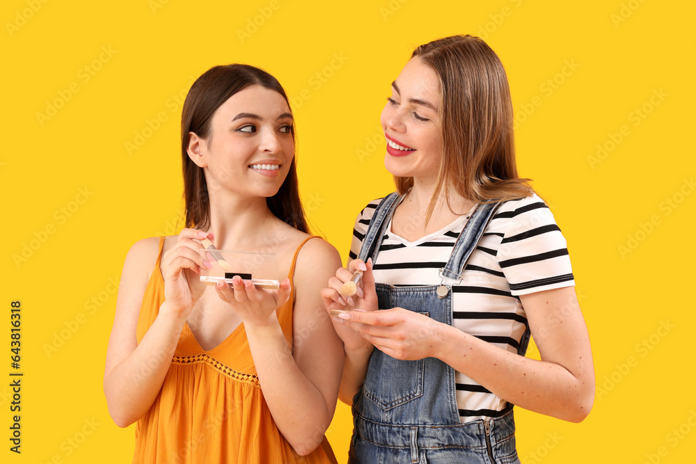 Female friends with decorative cosmetics on yellow background