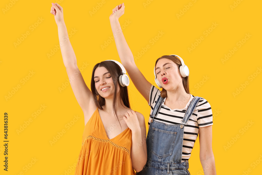 Female friends in headphones dancing on yellow background