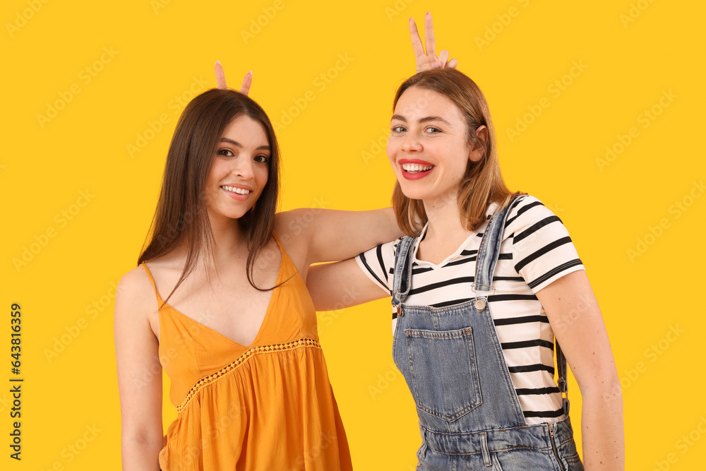 Female friends making horns on yellow background