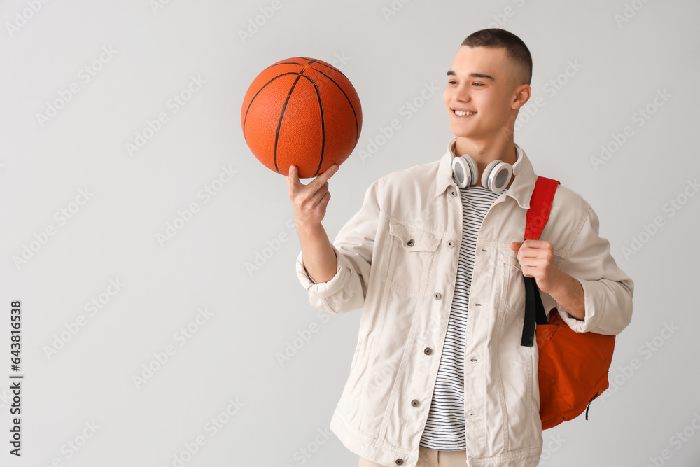 Male student with backpack, headphones and ball on grey background