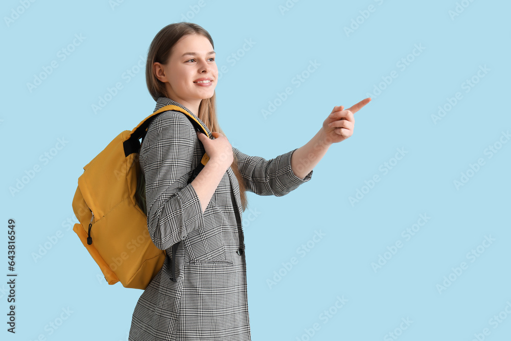 Female student with backpack pointing at something on blue background