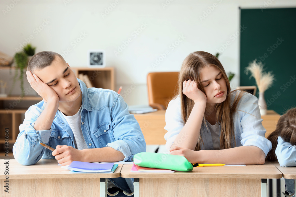 Tired sleepy classmates sitting at desks in classroom