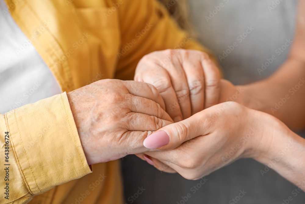 Senior woman with her granddaughter holding hands at home, closeup