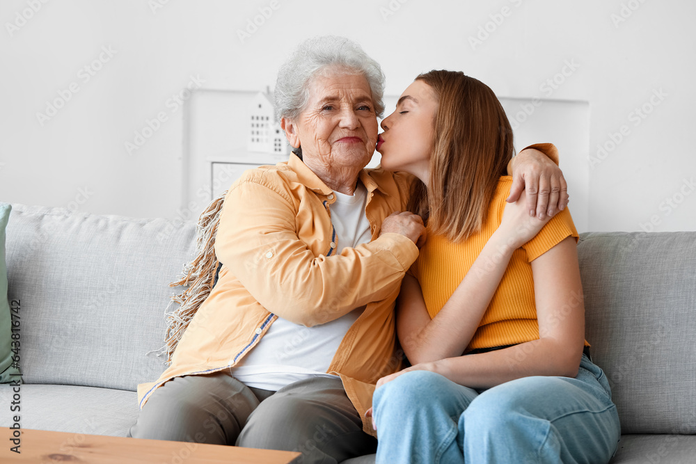 Young woman with her grandmother hugging on sofa at home