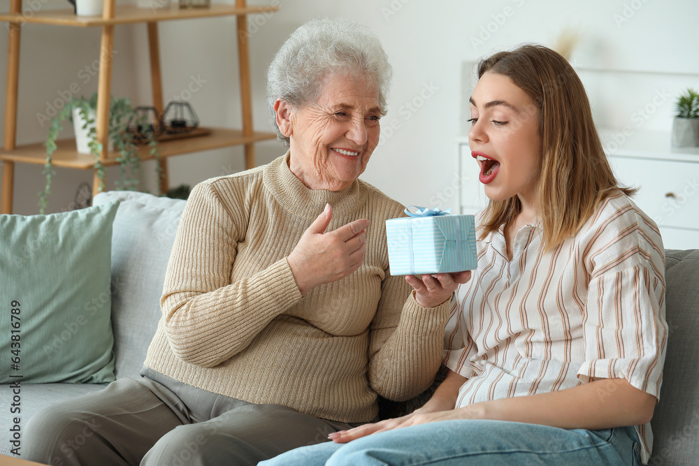 Senior woman greeting her granddaughter with gift at home