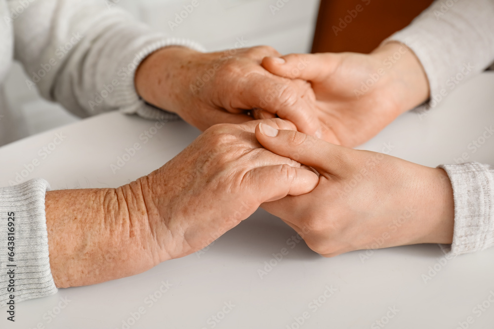 Young woman with her grandmother holding hands at table in kitchen, closeup