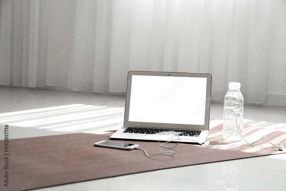 Laptop with mobile phone and earphones on fitness mat in gym