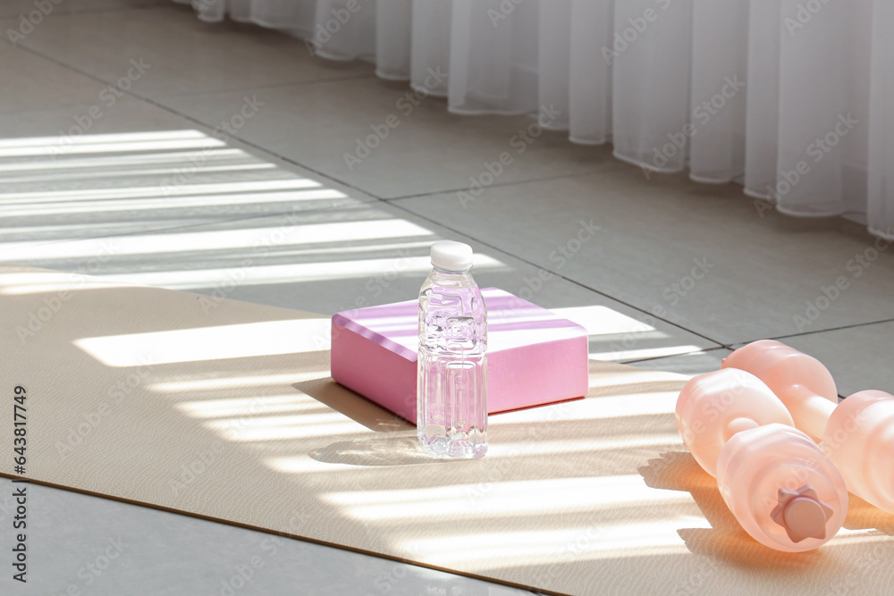 Bottle of water with dumbbells and block on fitness mat in gym