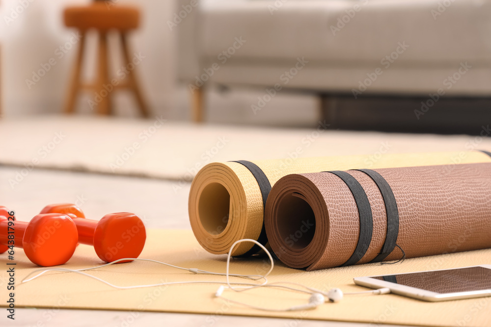 Tablet computer with earphones and dumbbells on fitness mat in living room