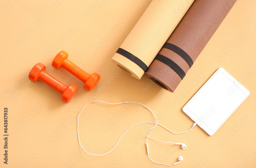 Tablet computer with earphones and dumbbells on fitness mat, top view