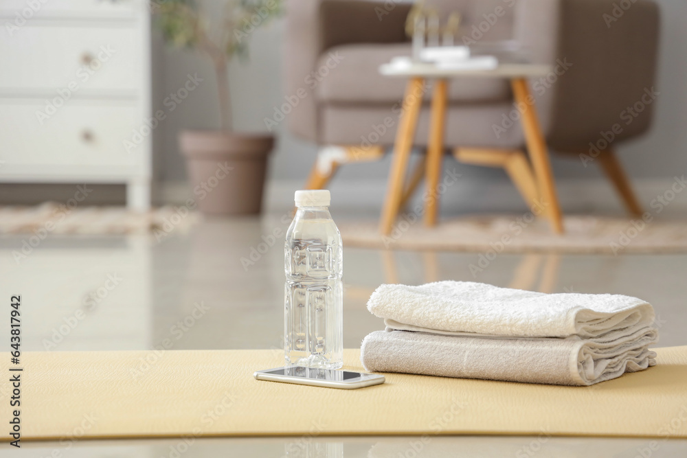 Mobile phone with bottle of water and towels on fitness mat in living room