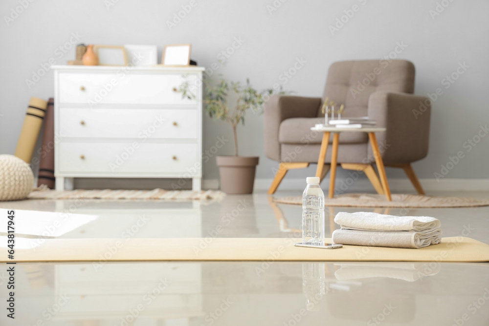 Mobile phone with bottle of water and towels on fitness mat in living room