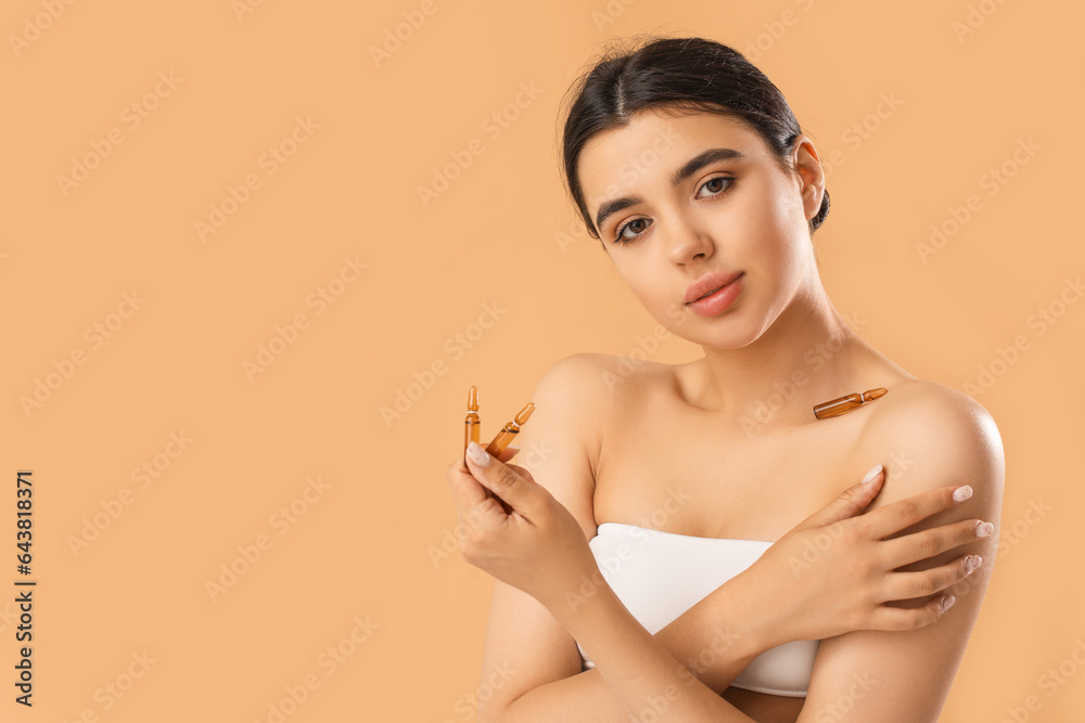 Beautiful young woman with ampules on beige background