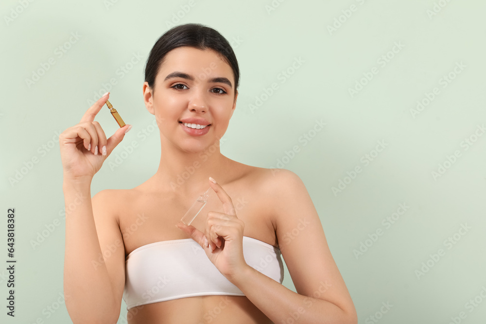 Beautiful young woman with ampules on green background