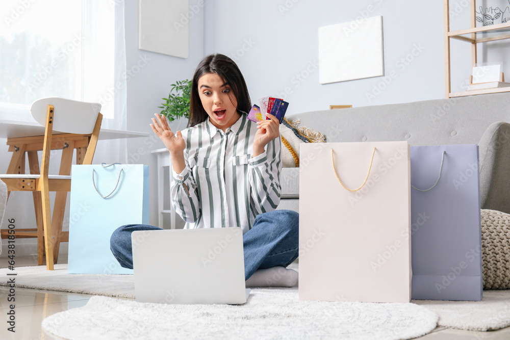 Surprised young woman with credit cards and laptop shopping online at home