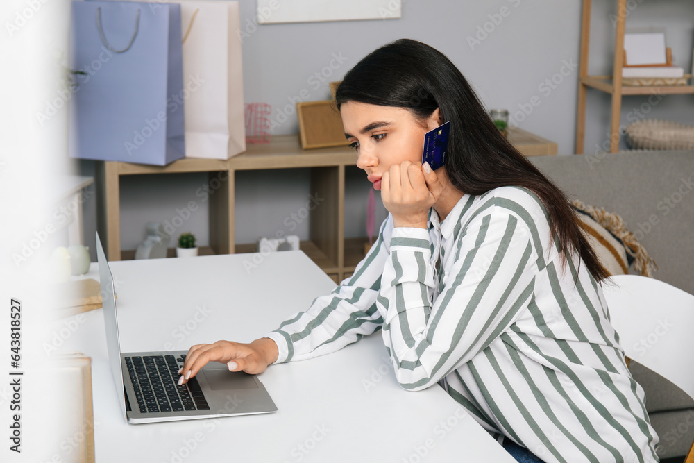 Upset young woman with credit card and laptop shopping online at home