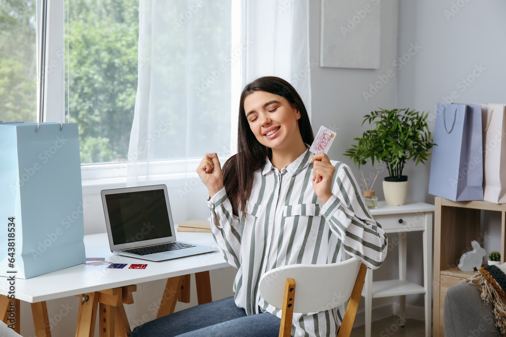 Happy young woman with gift card and laptop shopping online at home