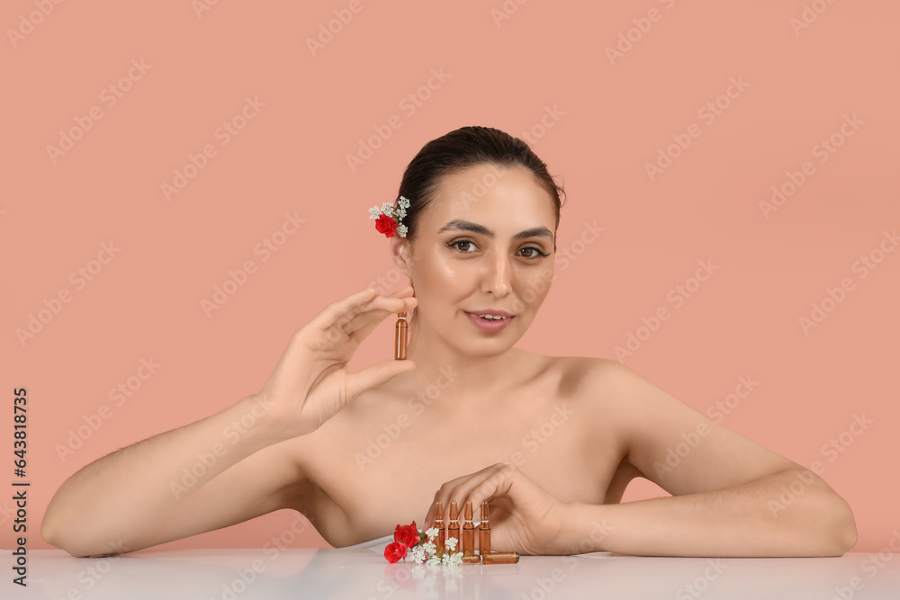 Beautiful young woman with flowers and ampules on table against pink background