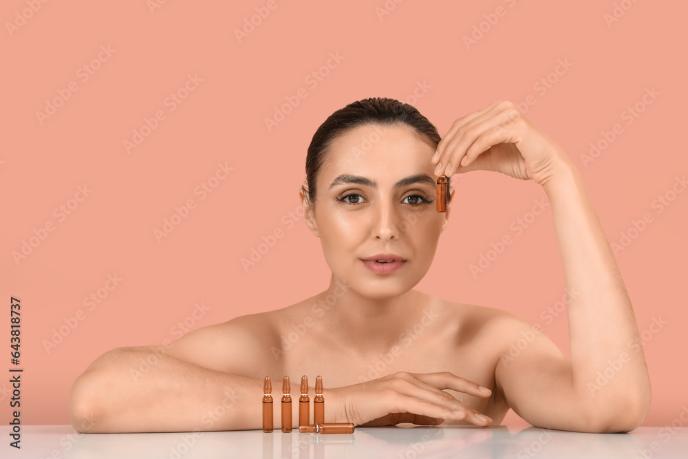 Beautiful young woman with ampules on table against pink background