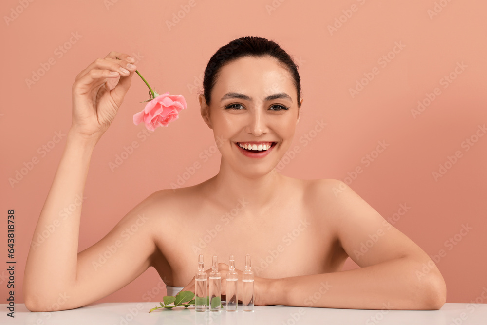 Beautiful young woman with rose and ampules on table against pink background