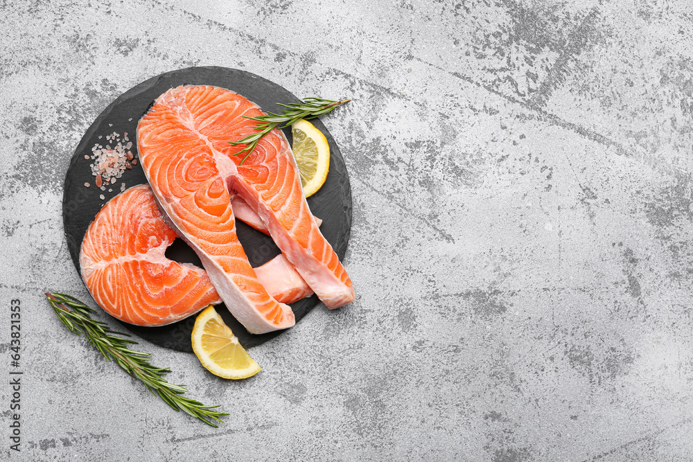 Wooden board with raw salmon steaks and different spices on blue background