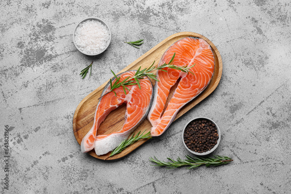 Wooden board with raw salmon steaks and different spices on blue background