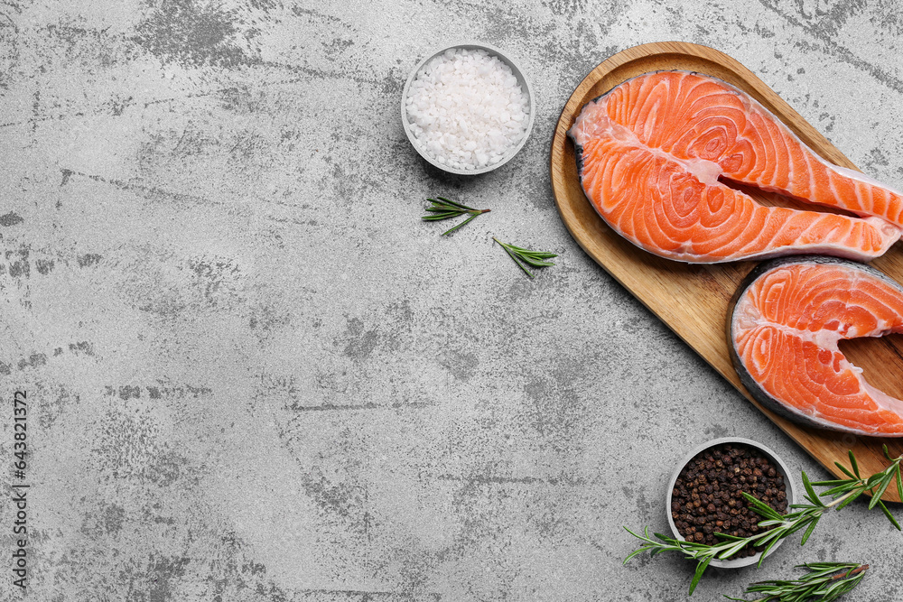 Wooden board with raw salmon steaks and different spices on blue background