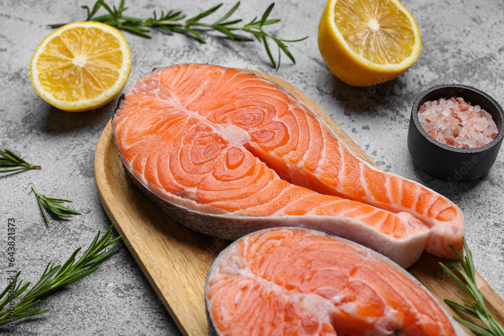 Wooden board with raw salmon steaks and different spices on blue background