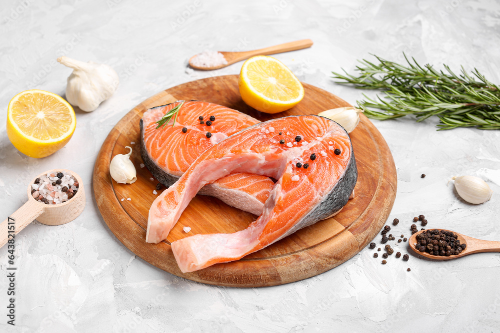 Wooden board with raw salmon steaks and different spices on grey background