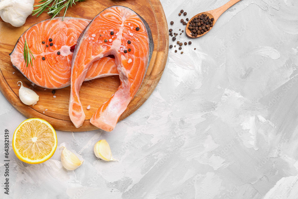 Wooden board with raw salmon steaks and different spices on grey background