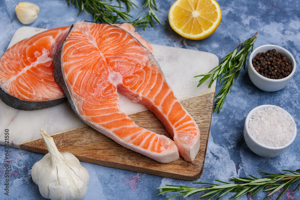 Board with raw salmon steaks and different spices on blue background