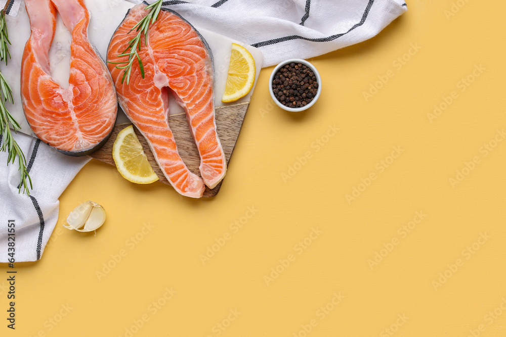 Board with raw salmon steaks and different spices on yellow background