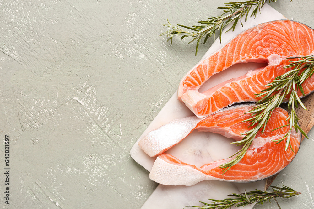 Board with raw salmon steaks and rosemary on grey background