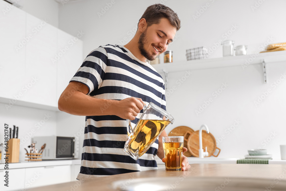 Young man pouring juice into glass in kitchen