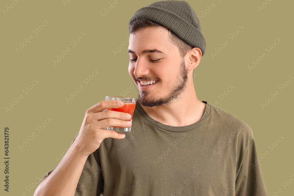 Young man with glass of tomato juice on green background, closeup