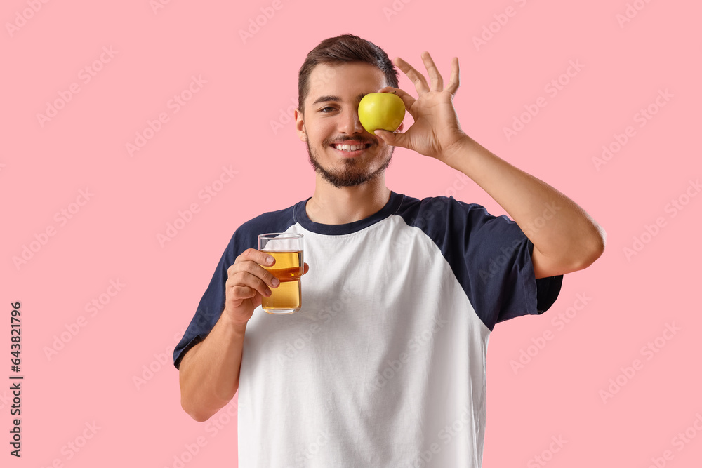 Young man with apple and glass of juice on pink background