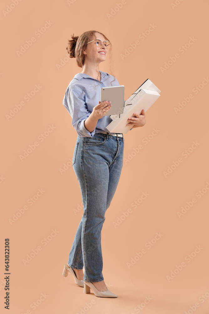 Young businesswoman with tablet computer and folders on beige background