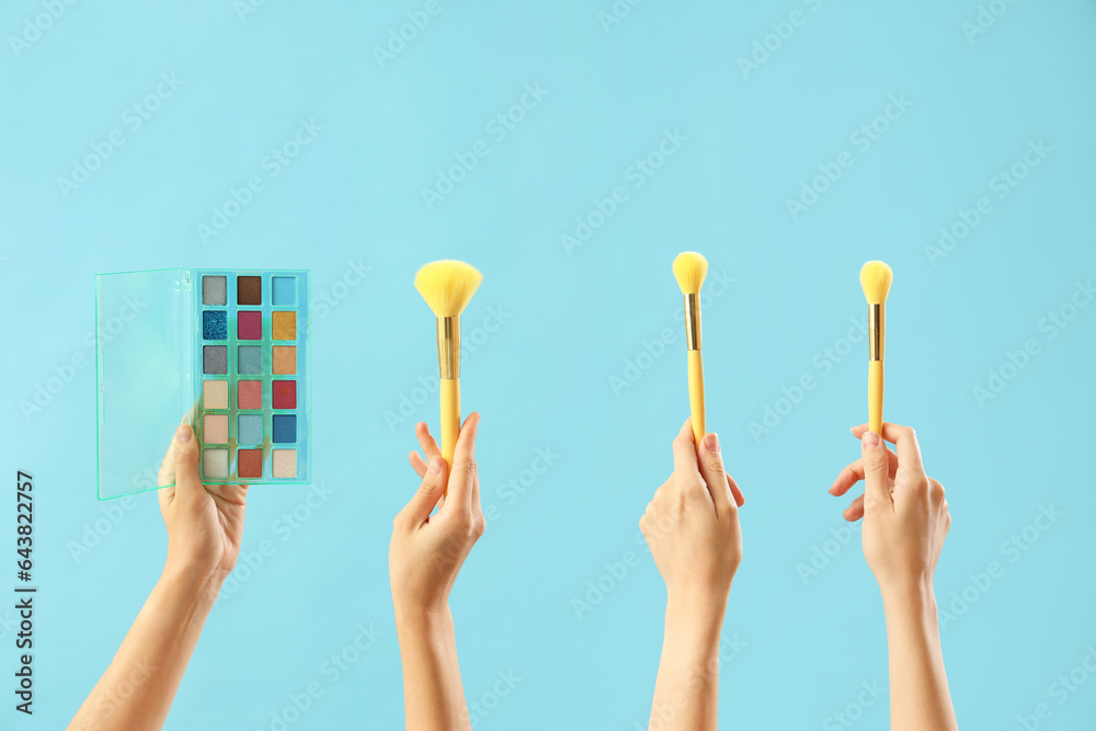 Women with makeup brushes and eyeshadows on blue background