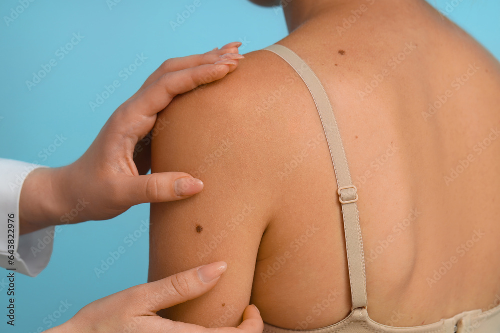 Dermatologist examining young womans mole on blue background, closeup