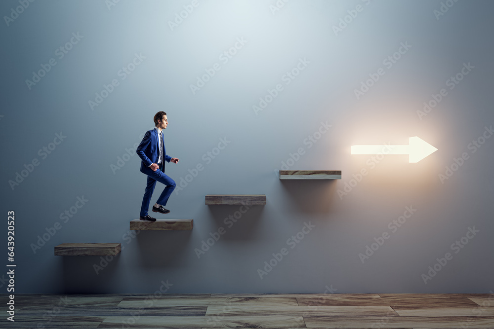 Side view of young male climbing illuminated arrow stairs to success on concrete wall background in 