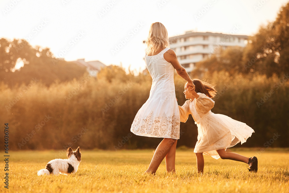 Dancing, having fun. Mother with her daughter and cute dog are on the field outdoors