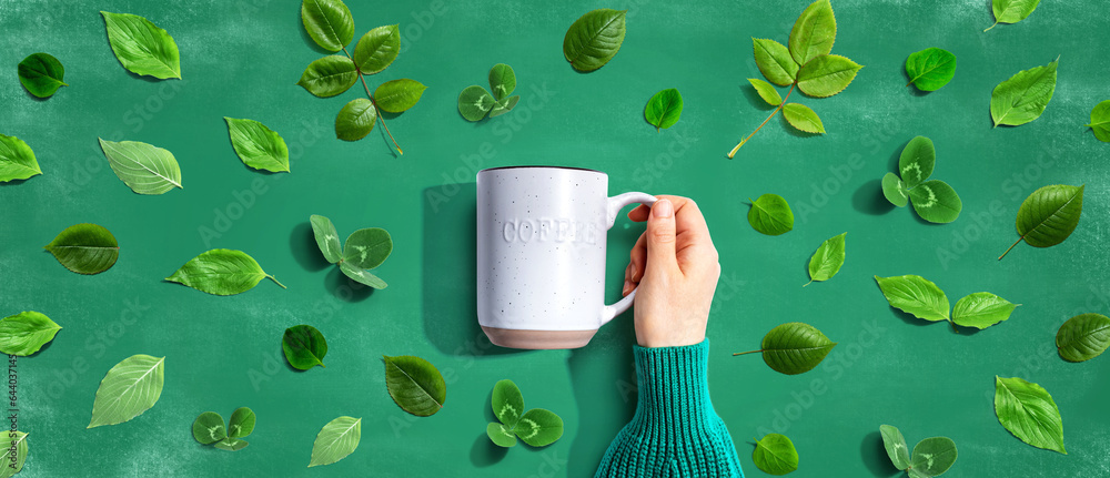 Person holding a mug with green leaves - flat lay