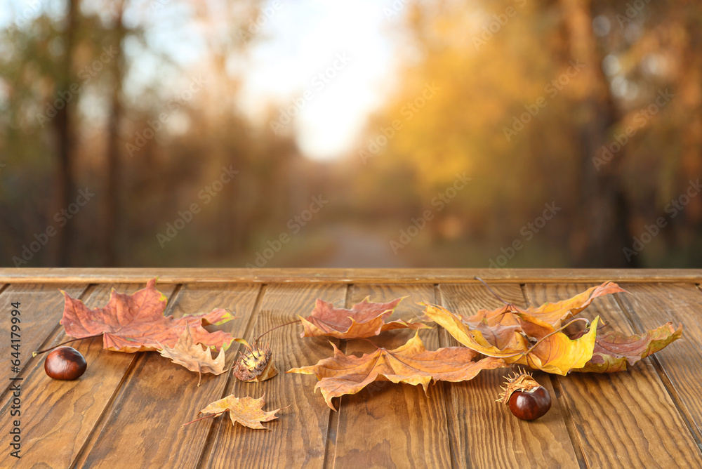 Dry autumn leaves and chestnuts on wooden table outdoors