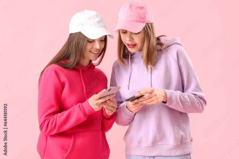 Female friends using mobile phones on pink background