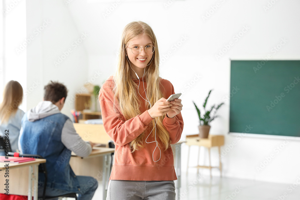 Female student with mobile phone and earphones in classroom