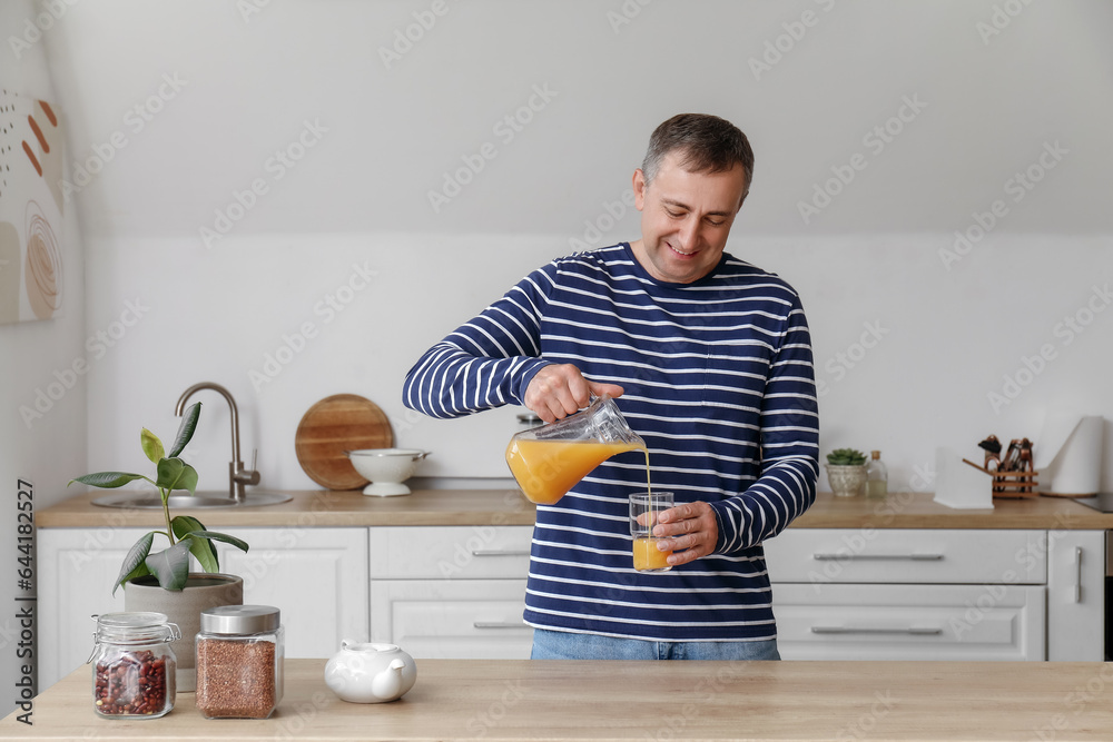 Mature man pouring orange juice into glass in kitchen