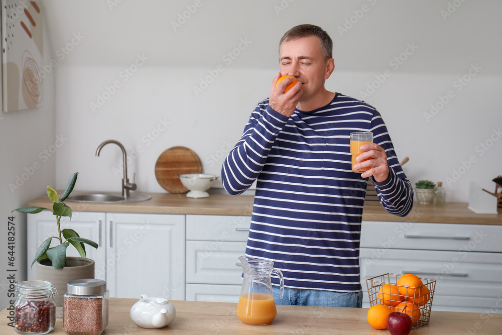 Mature man with glass of juice and orange in kitchen