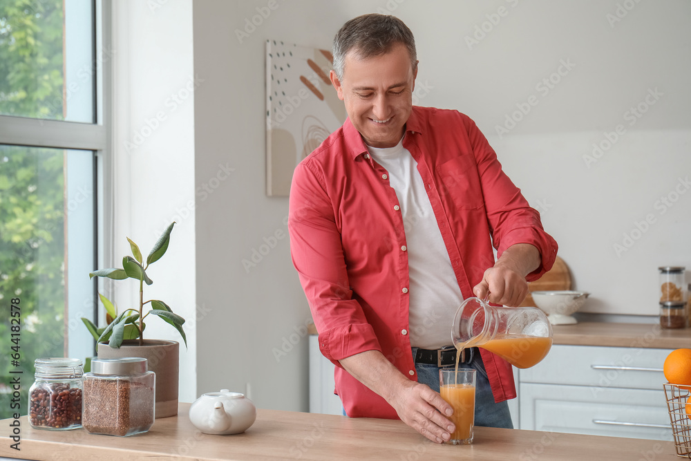 Mature man pouring orange juice into glass in kitchen