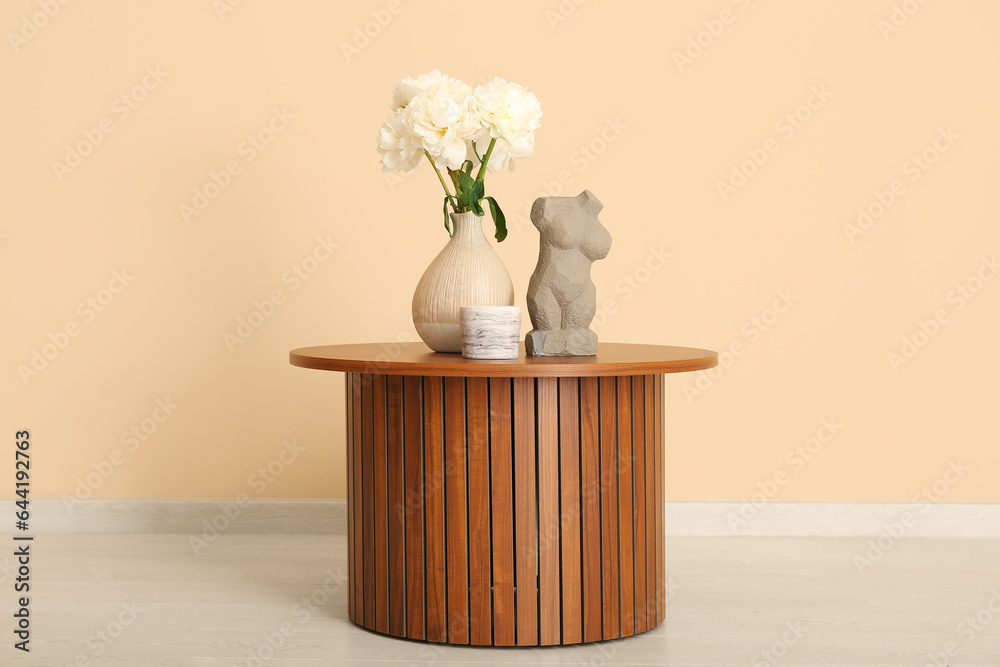 Vase of white peonies and figurine on coffee table near beige wall