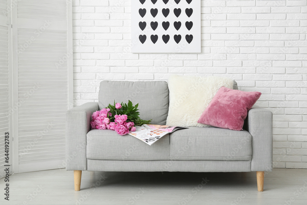 Bouquet of pink peonies with magazine and pillows on couch near white brick wall